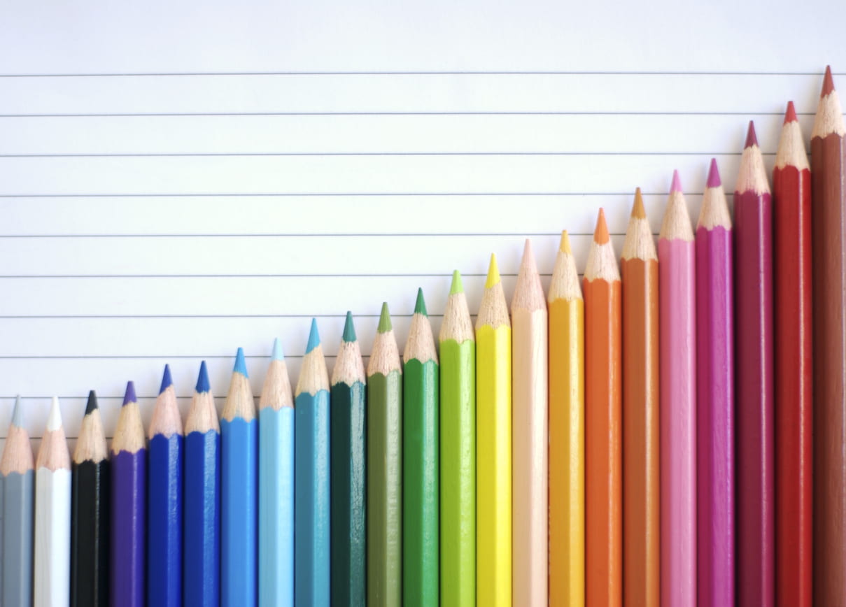 Bar chart graph rainbow of colored pencils slide up against a sheet of lined paper sloping in a good direction of success